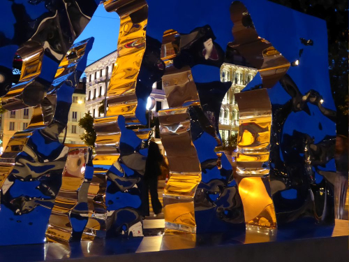 Skulptur als spiegelnder Schriftzug vor Häuserzeile, Schweiz