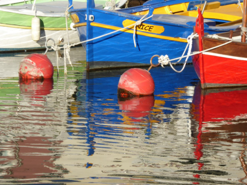 Farbenfrohe Boote und Bojen spiegeln sich im Wasser