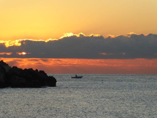 Fischerboot im Sonnenaufgang mit Wolkenband am gelb orangenem Himmel in Nizza