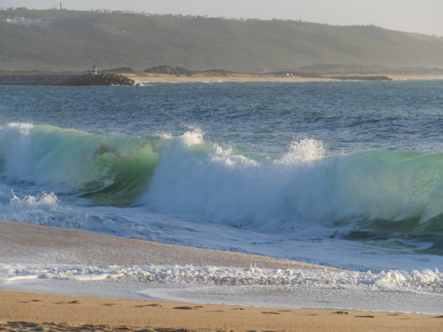 Heranrollende Welle mit Wind und Weißwasser mit Blick auf den Hafen in Nazare