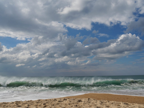 Sandstrand, bewegtes Meer mit Welle und weißen Wolken in Nazare